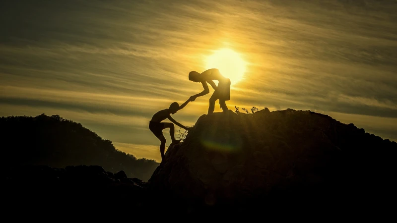 man helping another man up a mountain