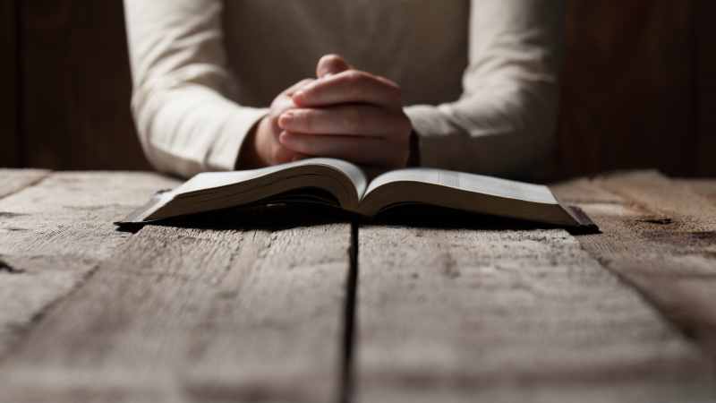 man sitting at a table praying behind a bible