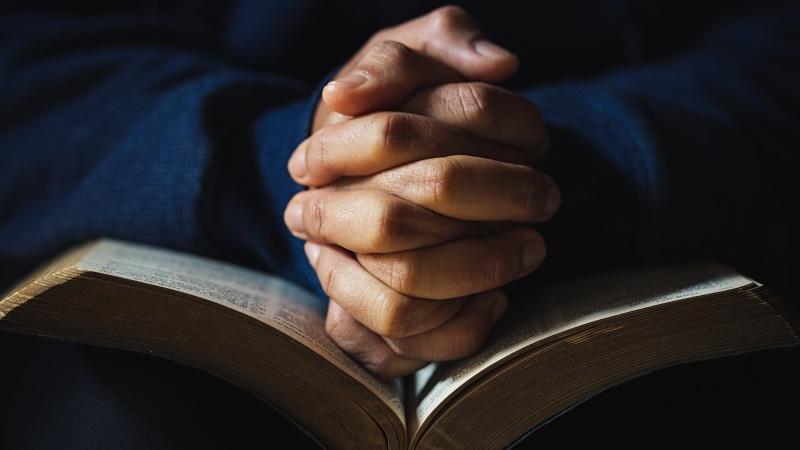 man with hands praying on bible