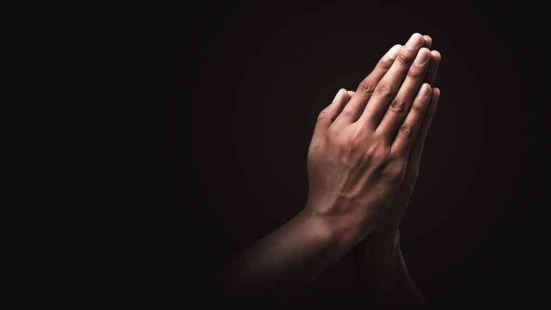Hands folded in prayer with black backgound