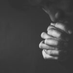 man folding hands praying in the darkness