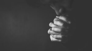 man folding hands praying in the darkness