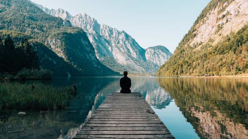 رجل يجلس على رصيف على بحيرة هادئة محاطة بالجبال