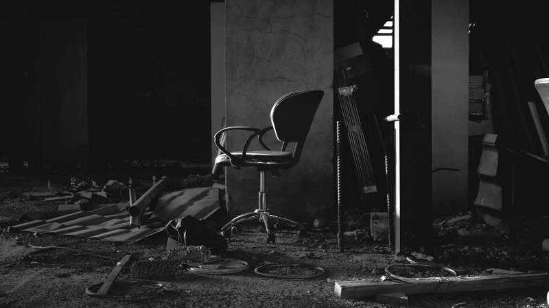black and white dark photo of a chair in a messy and dark room