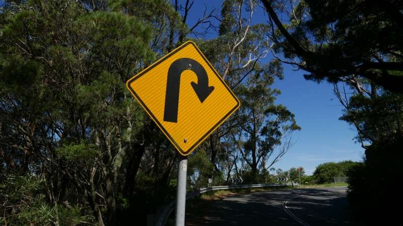 uturn sign with trees behind it