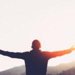 man with arms out wide praising God in sun