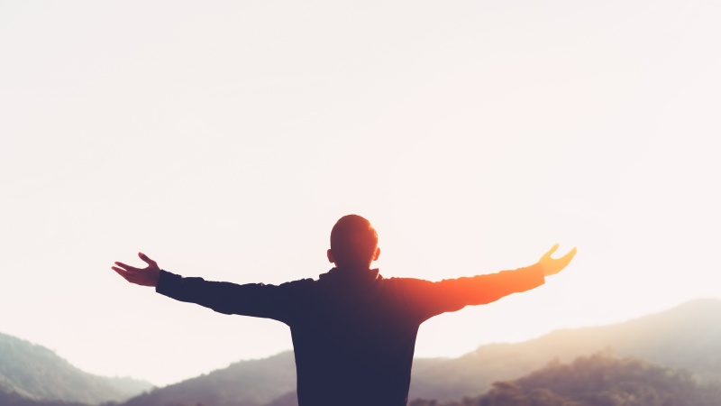 man with arms out wide praising God in sun